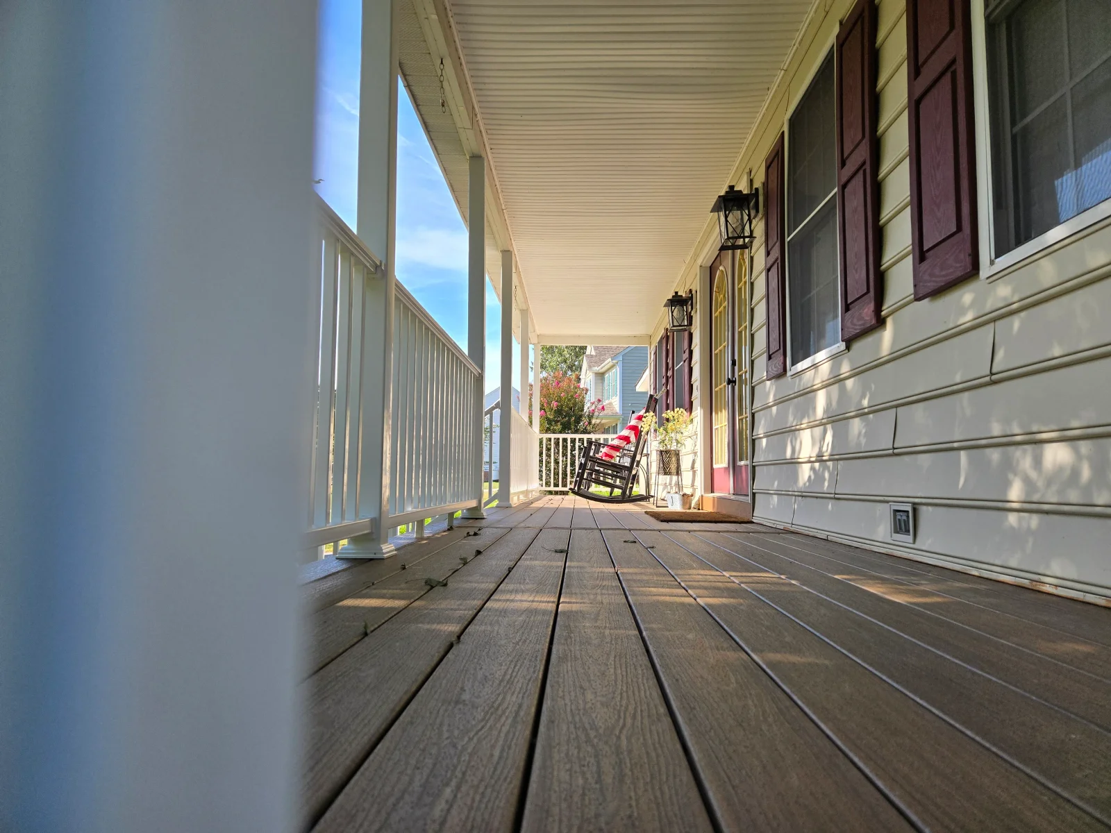 Covered porch with gray composite decking, white railing and columns, beadboard ceiling, and cream vinyl siding