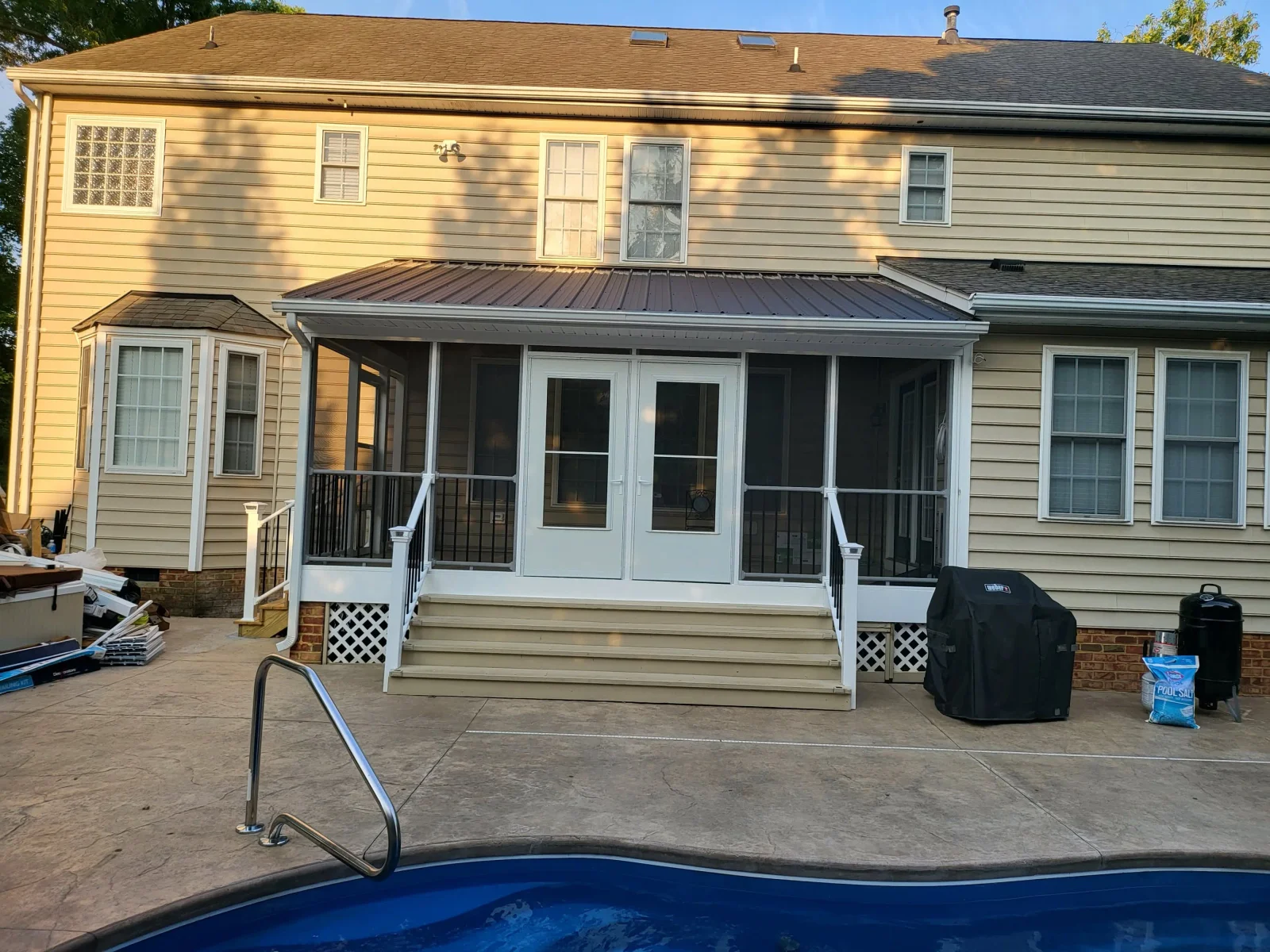 Screened porch with brown metal roof, white trim, white French doors, black metal railings, and tan decking steps