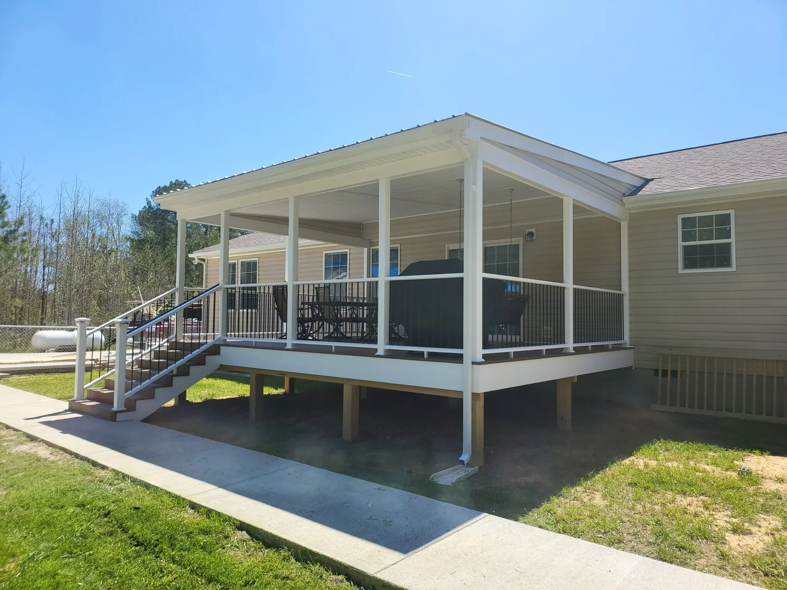 Raised covered deck with white vinyl posts, black metal balusters, metal roof, and composite stair treads