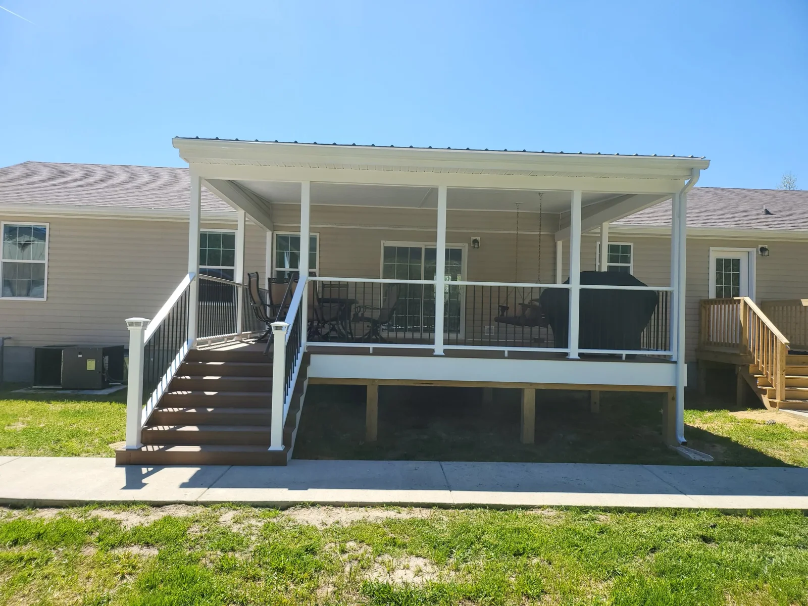 Covered back deck with brown composite boards, white vinyl posts and railing, black metal balusters, and white roof trim