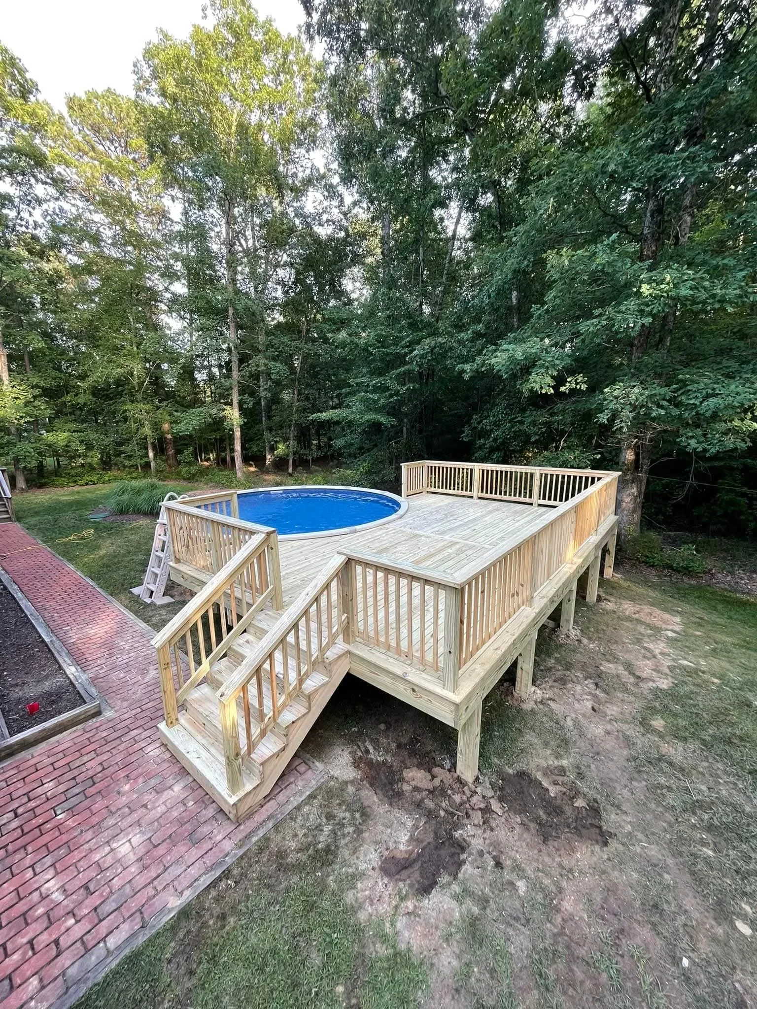 Pressure-treated wood deck with vertical baluster railings and staircase surrounding a round above-ground pool