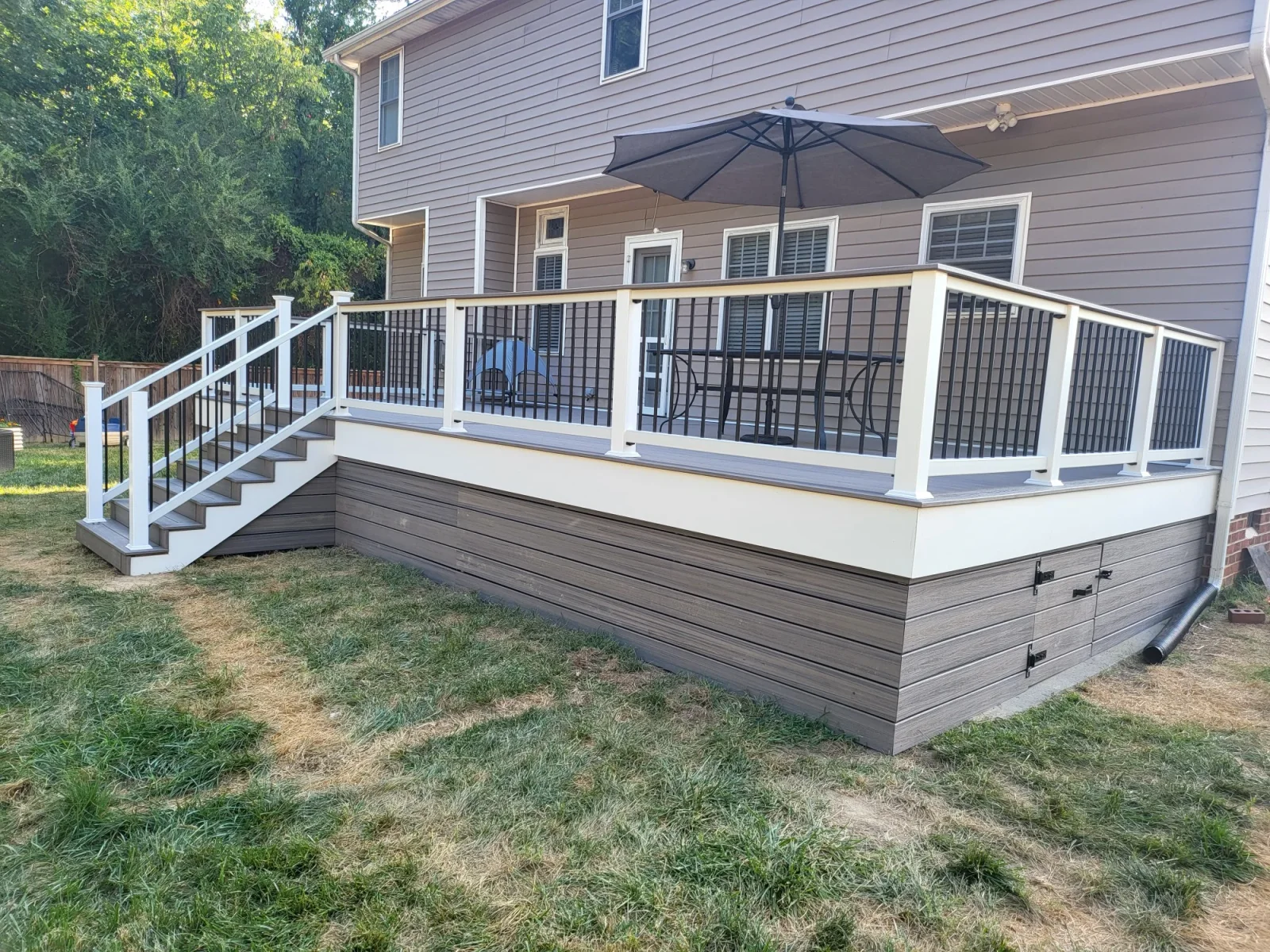 Raised composite deck with white rails, black metal balusters, and gray-brown composite skirting with access panel