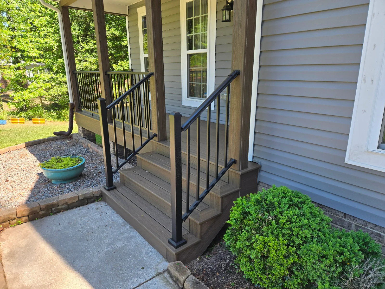 Brown composite porch steps with black aluminum railings, square balusters, and wood-grain composite porch columns