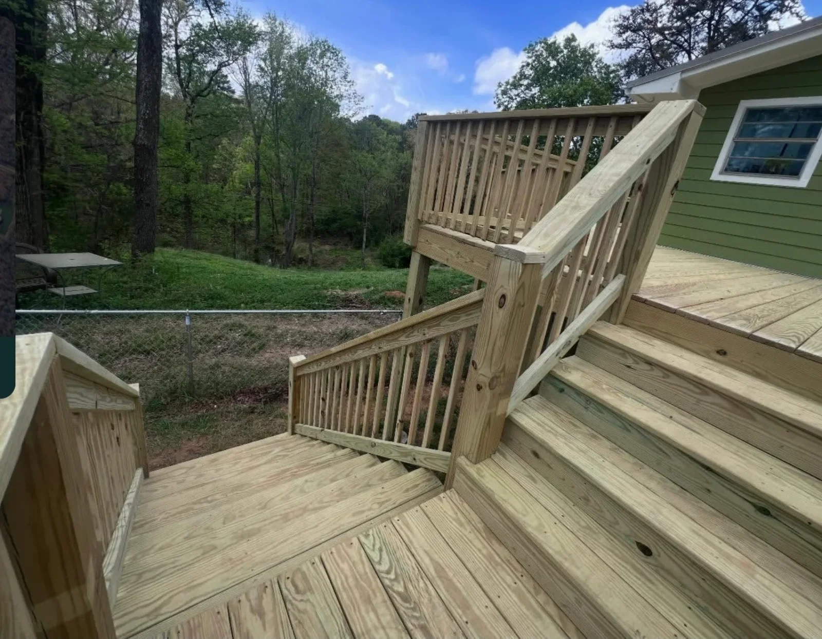 Pressure-treated wood deck with multi-step stair, vertical baluster railing, and handrail with square posts