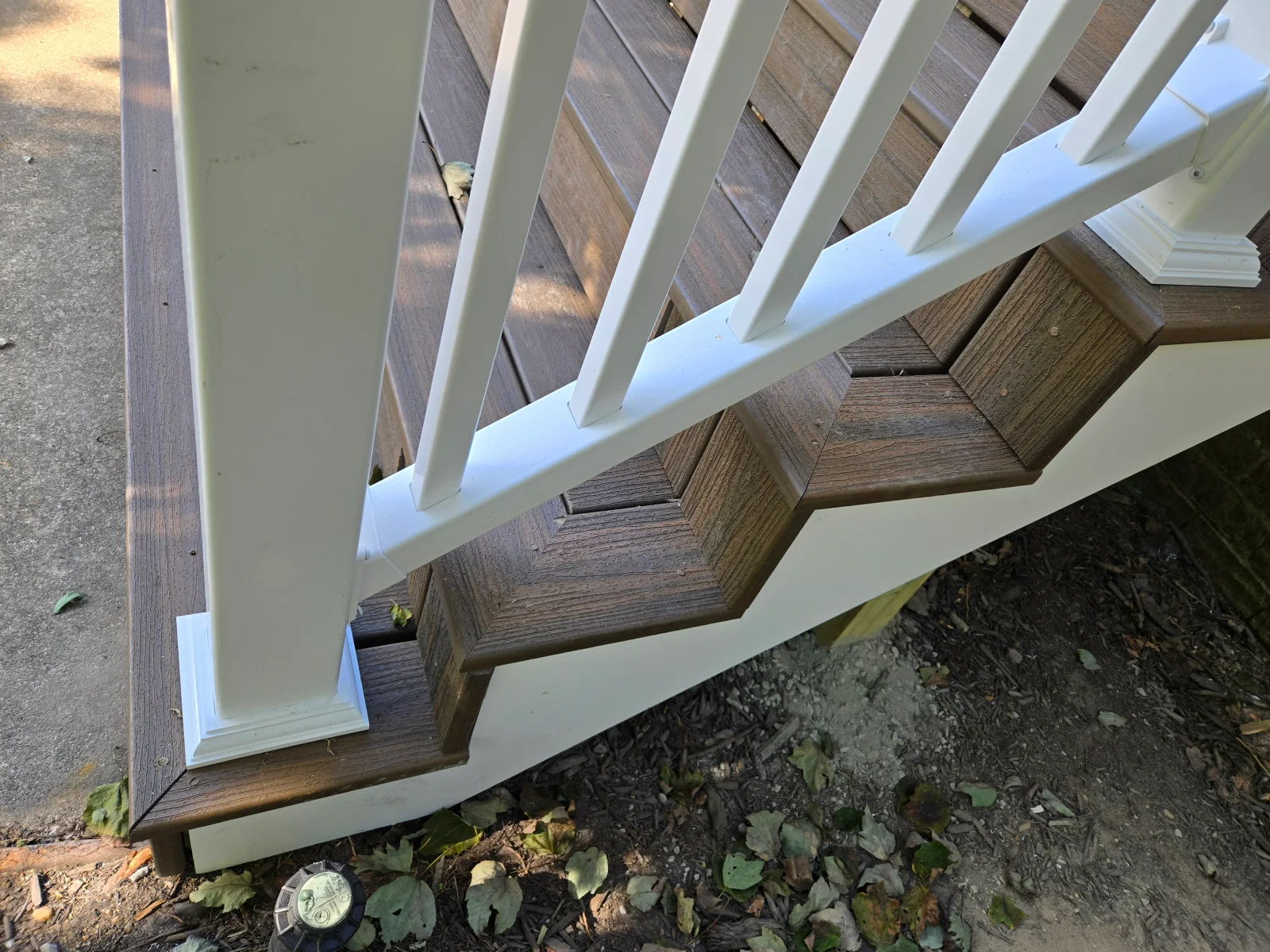 Brown composite deck stairs with white vinyl railing, square balusters, and post base trim