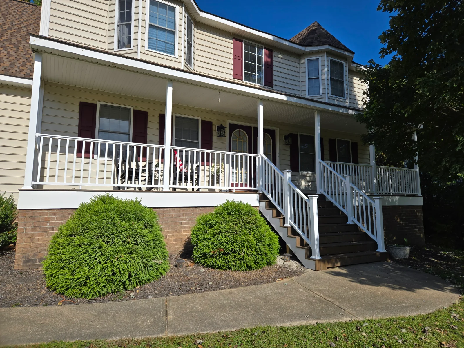 Covered front porch with white vinyl railing, white posts, and dark brown stair treads leading to a concrete walkway