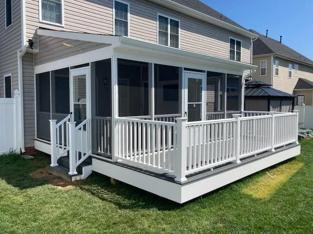 Screened porch with white frame and door over gray composite deck with white railings and steps, beside beige vinyl siding