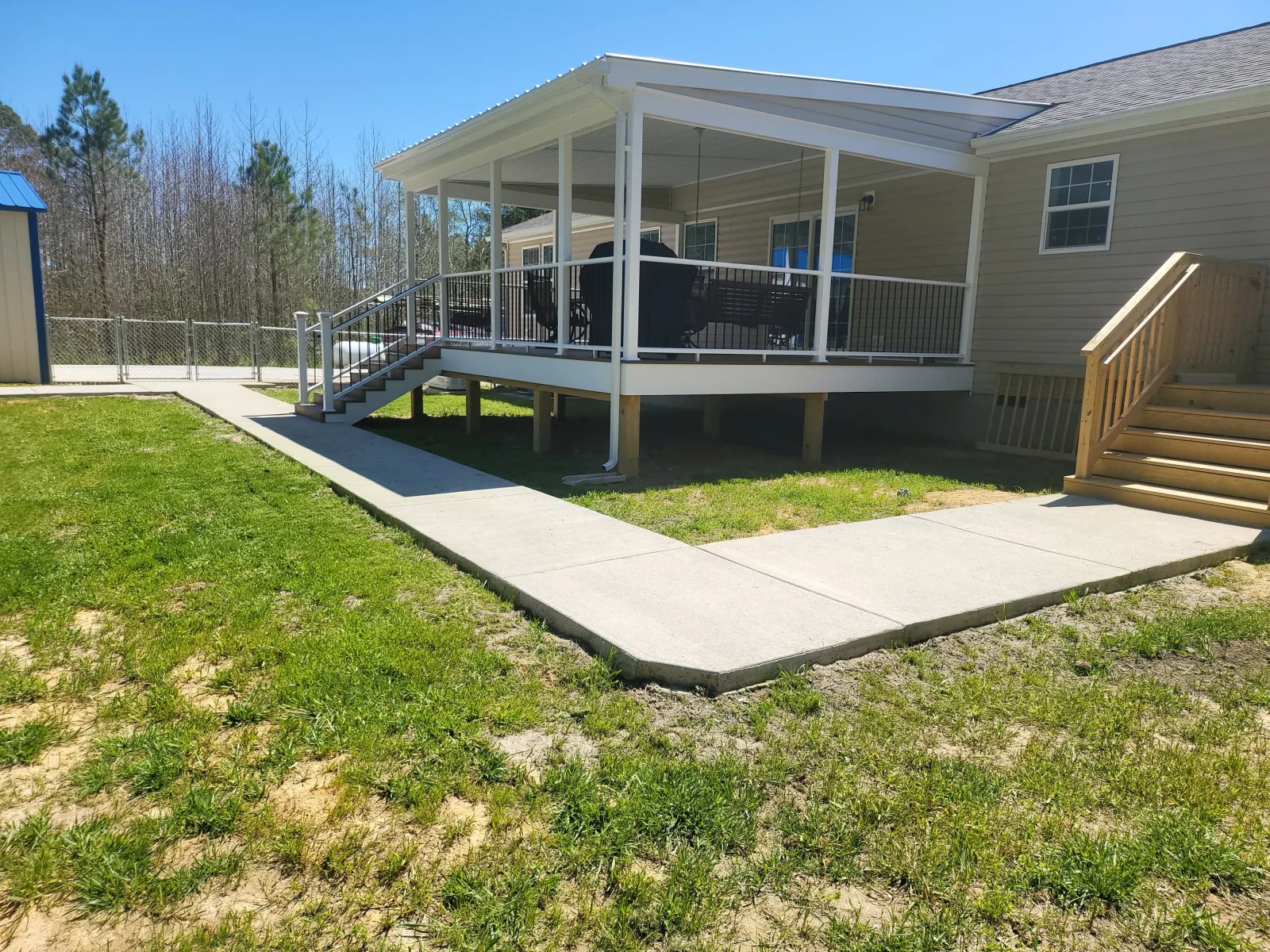 Covered raised deck with white railings, dark metal balusters, and wood stairs, plus a broad concrete walkway.