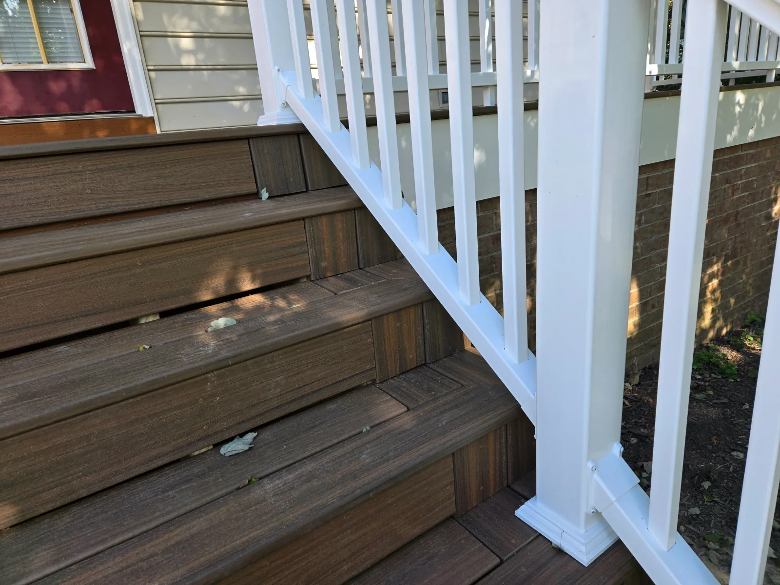 Dark brown composite deck stairs with white vinyl railing, square balusters, and newel post trim