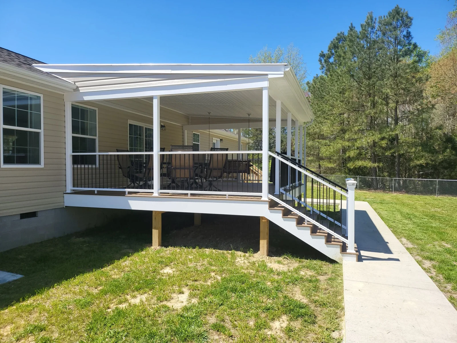 Covered back deck with white vinyl posts, black metal balusters, brown decking, and white stair railing