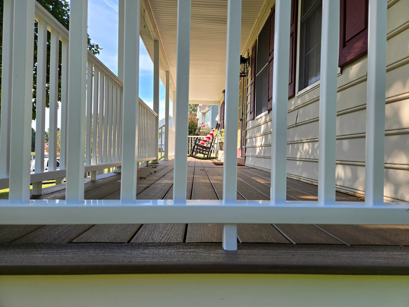 Composite porch deck with white vertical baluster railing and gray-brown decking boards beside cream siding