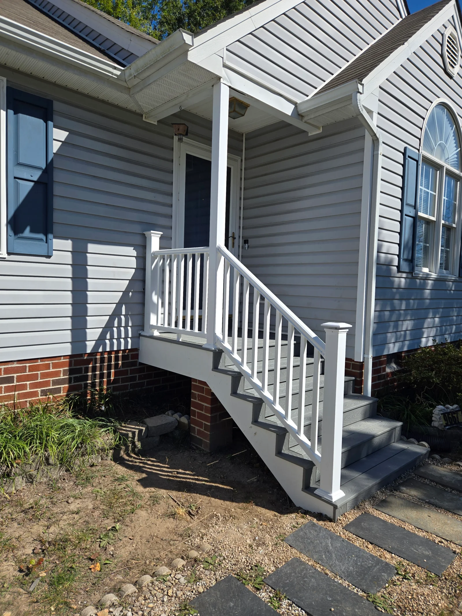 Gray composite front porch deck with white vinyl railing, square balusters, and matching staircase beside gray vinyl siding