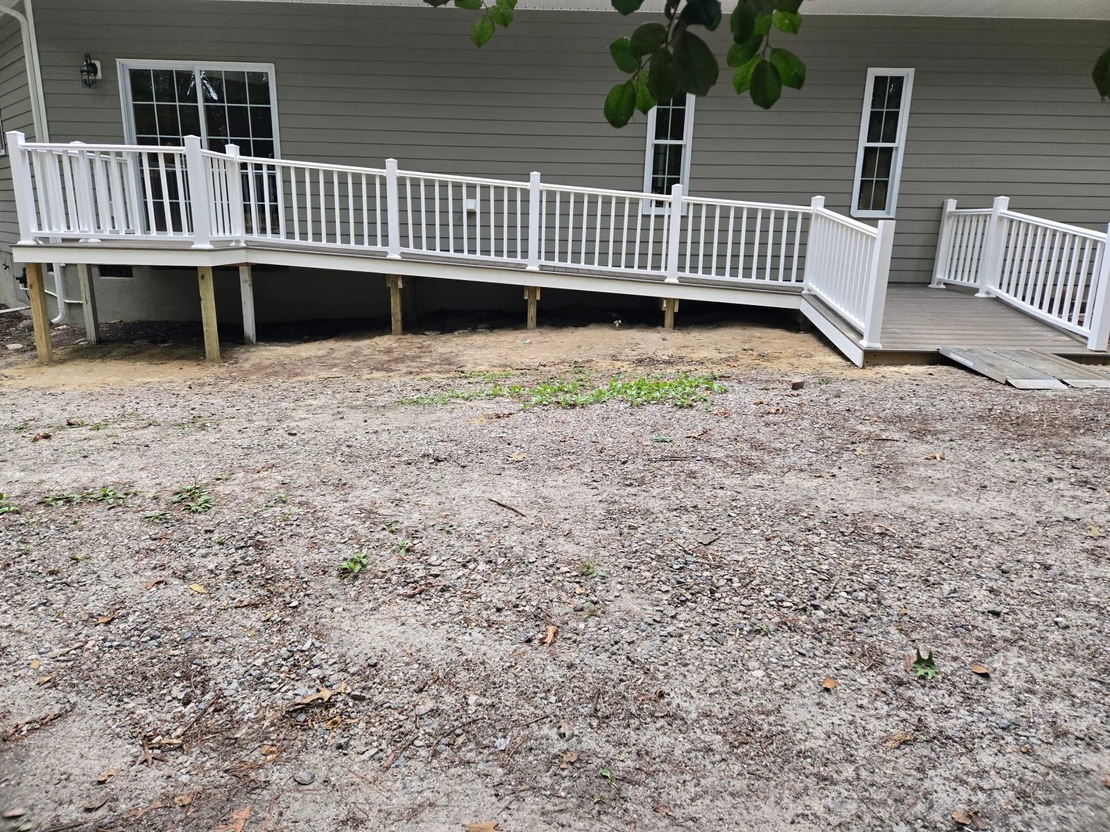 Raised deck with white vinyl railing, pressure-treated support posts, and stairs along a gray lap-siding home