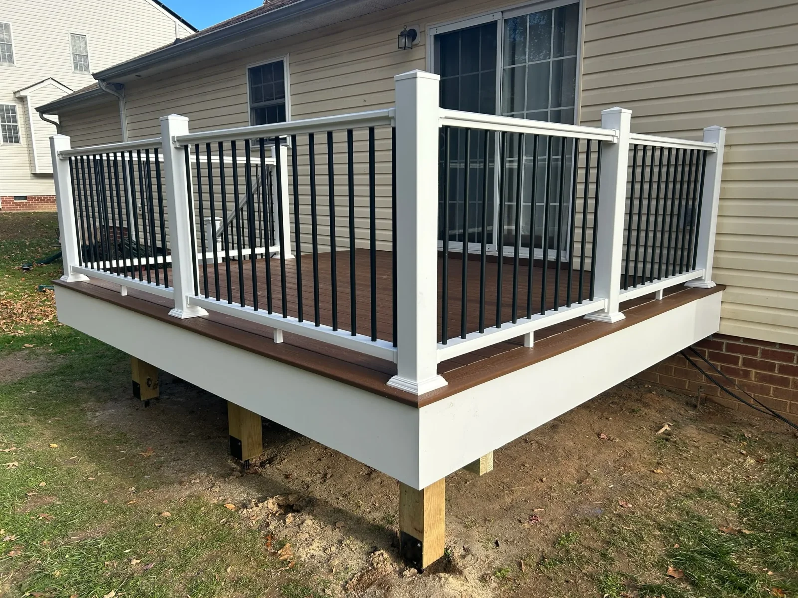 Brown composite deck with white vinyl railing and black aluminum balusters attached to a beige vinyl-sided house