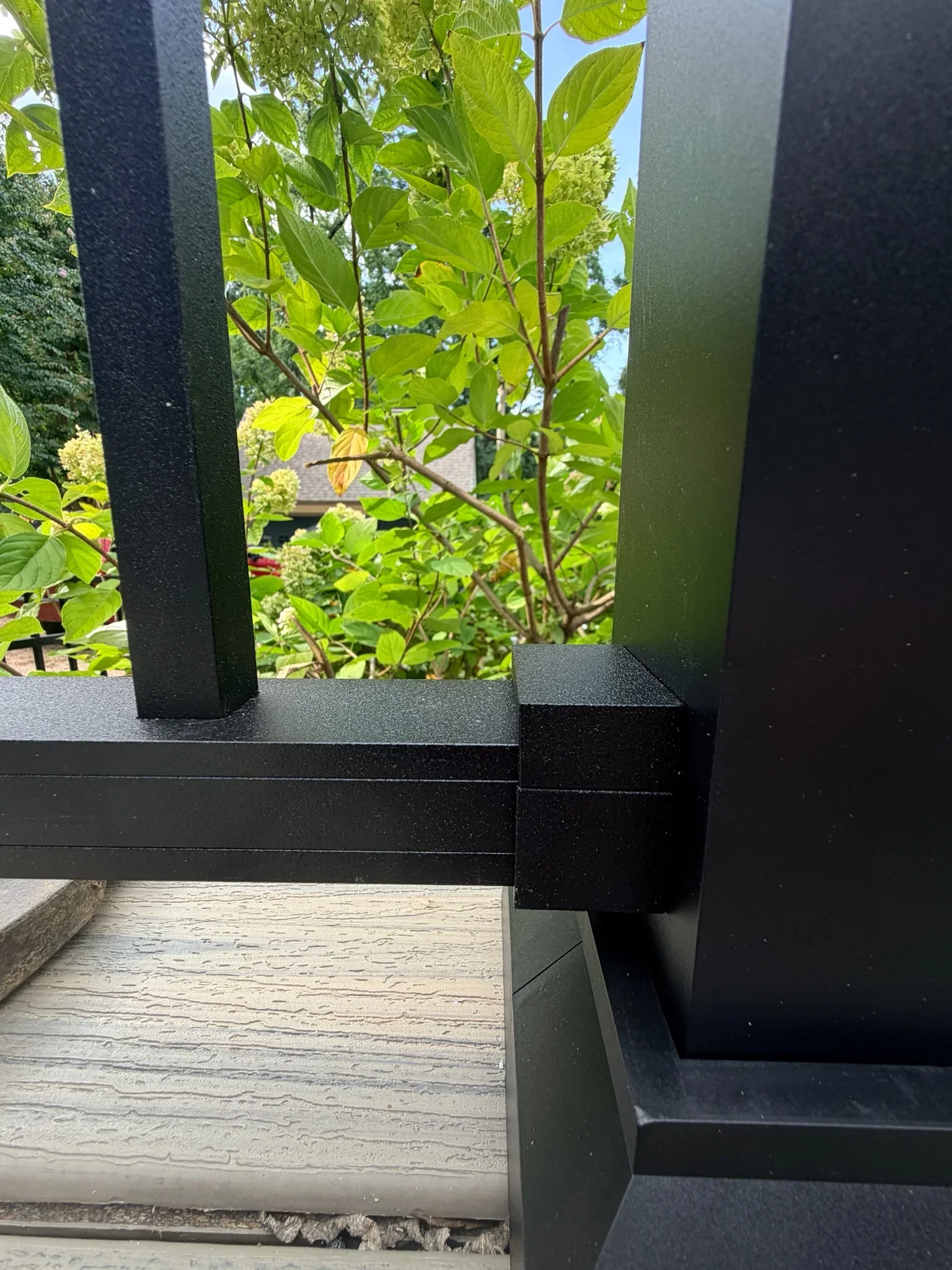 Black powder-coated aluminum railing with square posts and corner bracket over gray composite deck boards