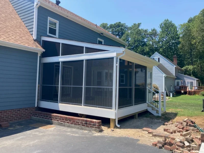 Screened porch addition with white aluminum frame, screen panels, raised wood deck, and black metal stair railing on blue lap siding home