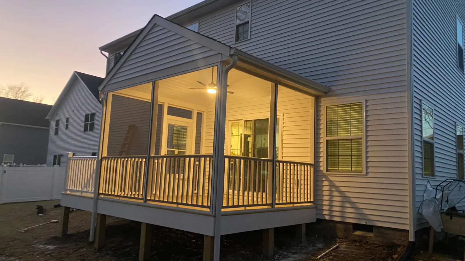 Screened-in porch with gabled roof, white trim, dark railings, and wood support posts beside vinyl-sided home