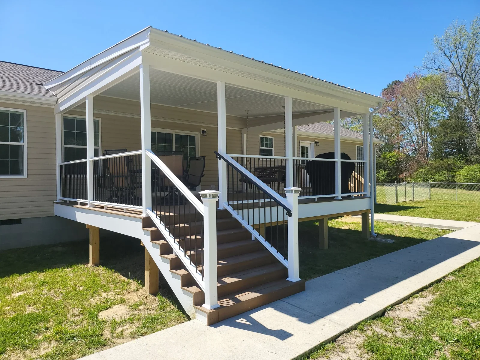 Covered deck with dark brown decking, white vinyl posts, black metal balusters, and white-trimmed roof over stairs and porch