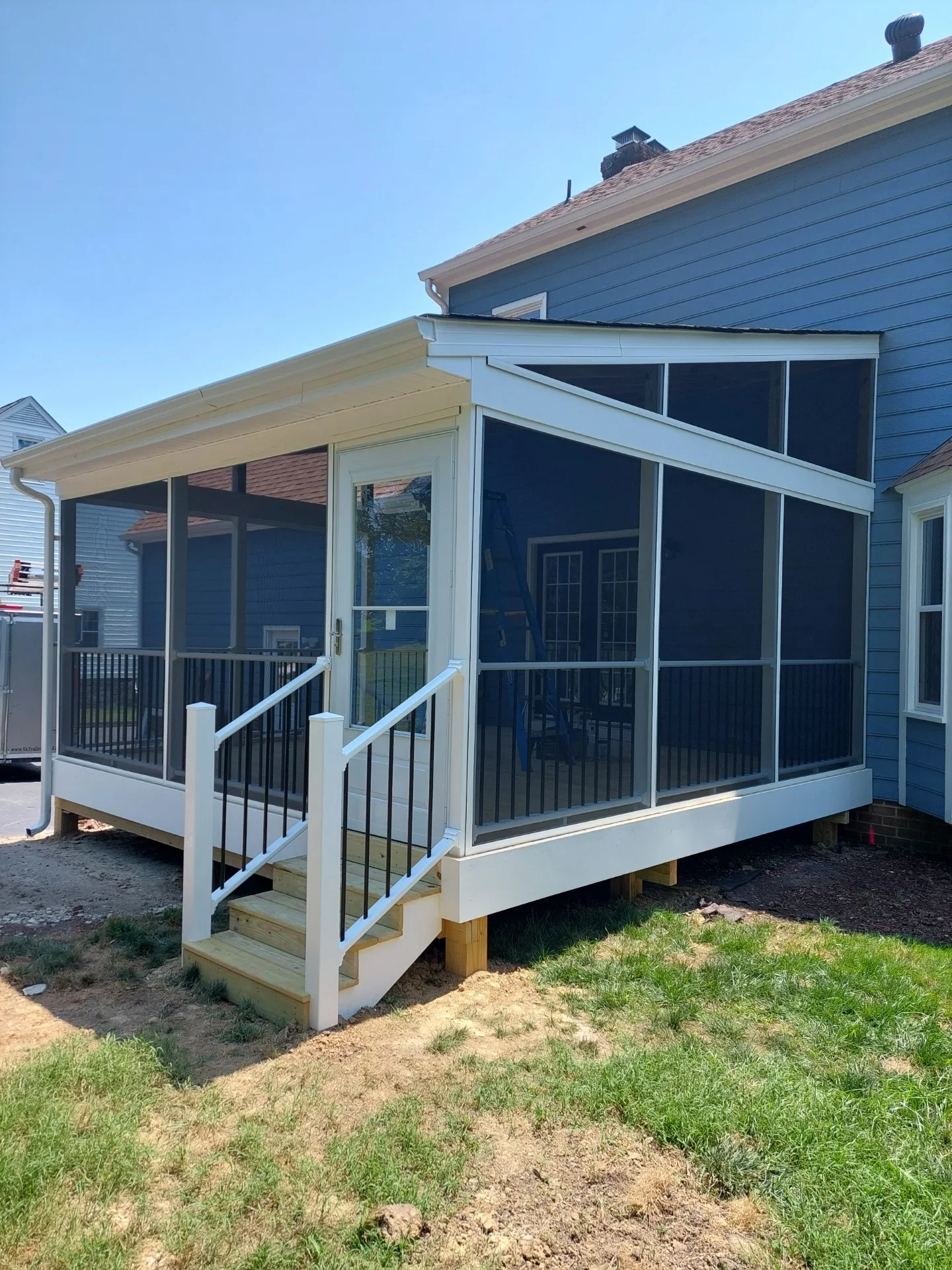 Screened porch with white vinyl trim, black aluminum railing, and pressure-treated wood steps