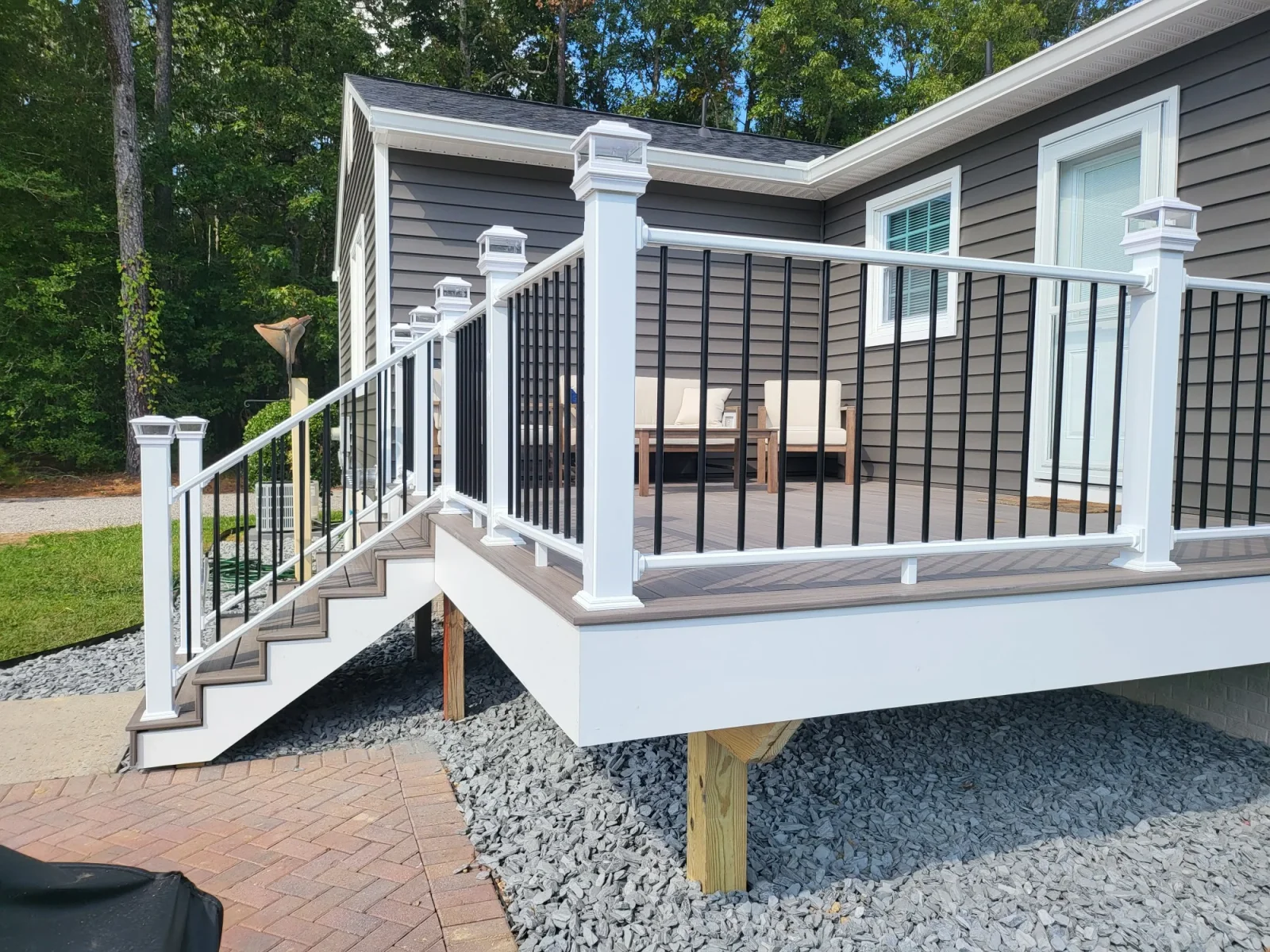 Raised composite deck with white railing, black balusters, post-cap lights, and matching stair run over gray gravel